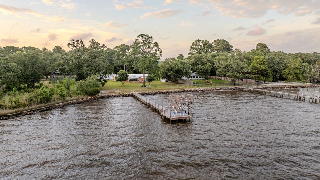 Aerial view at dusk of the dock and covered sundeck reaching into Choctawhatchee Bay, with the home and lawn behind