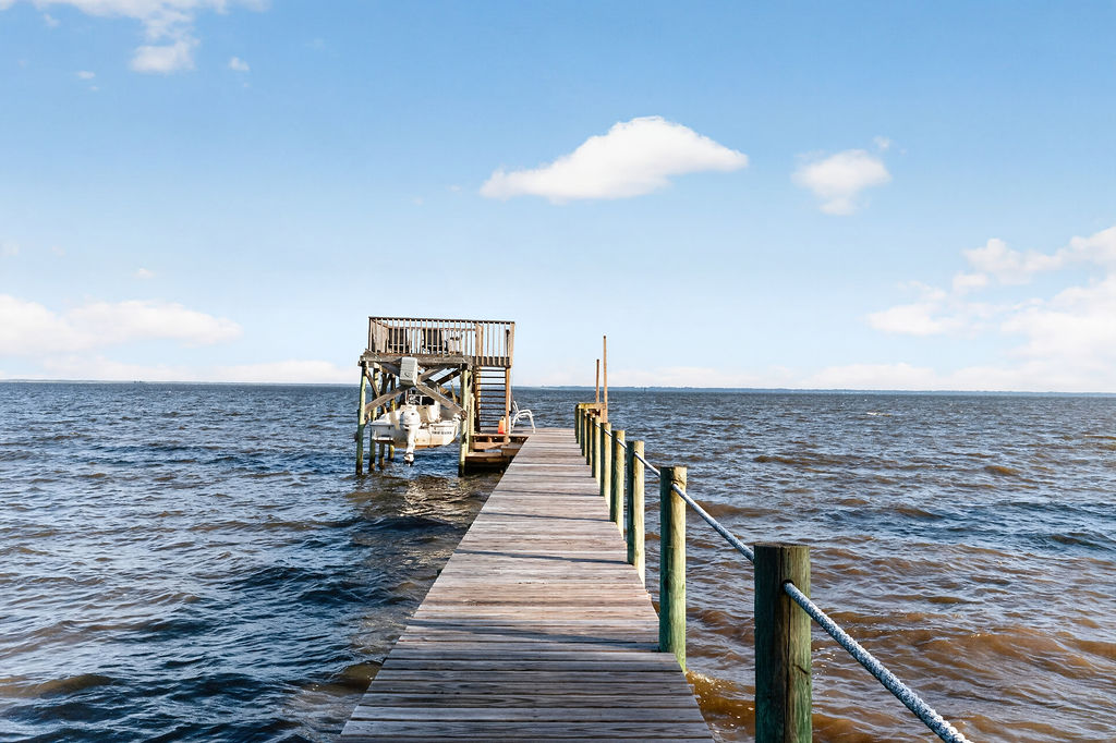 The 120-foot private dock running straight out over open bay water to a covered sundeck platform