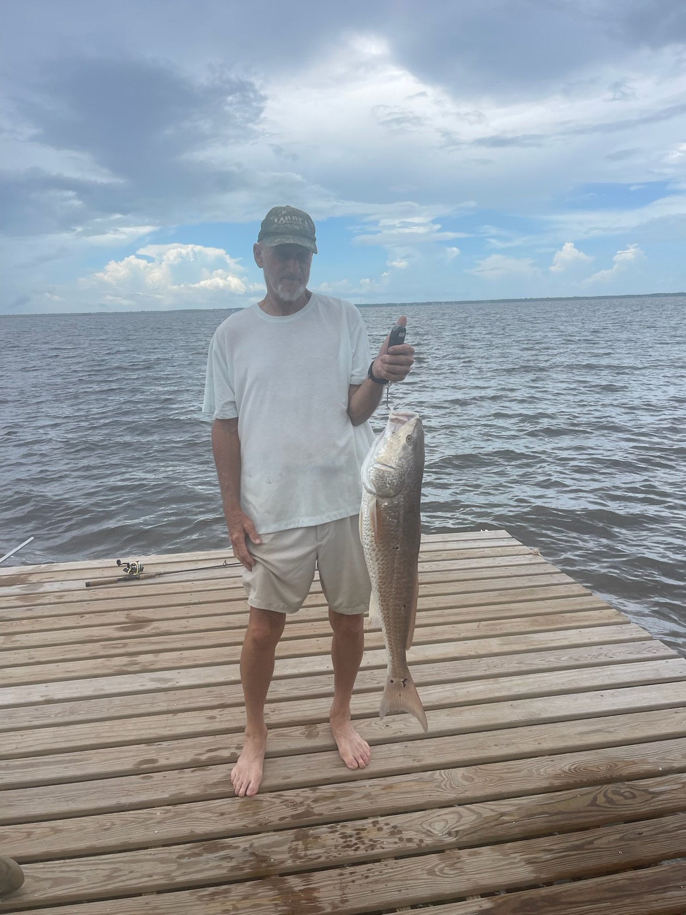 A large redfish caught and held up on the dock, bay water and cloudy sky behind