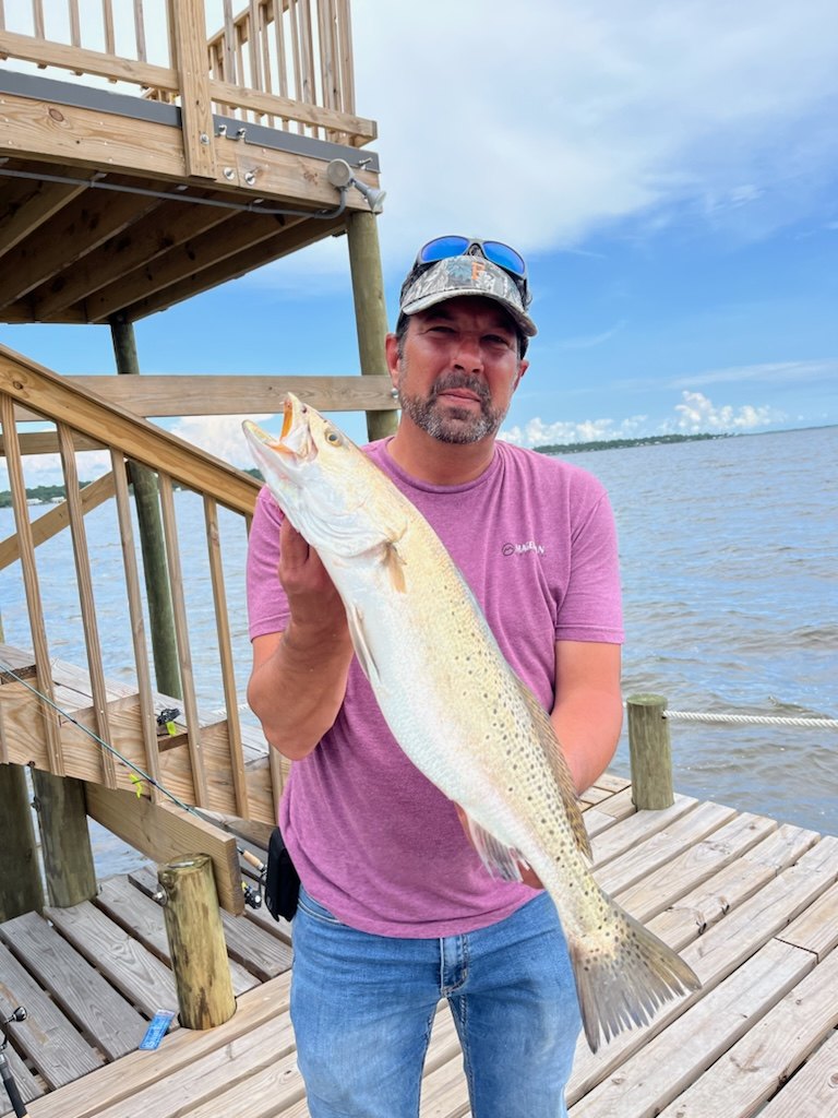 A speckled trout held up on the dock beside the sundeck stairs, bay in the background