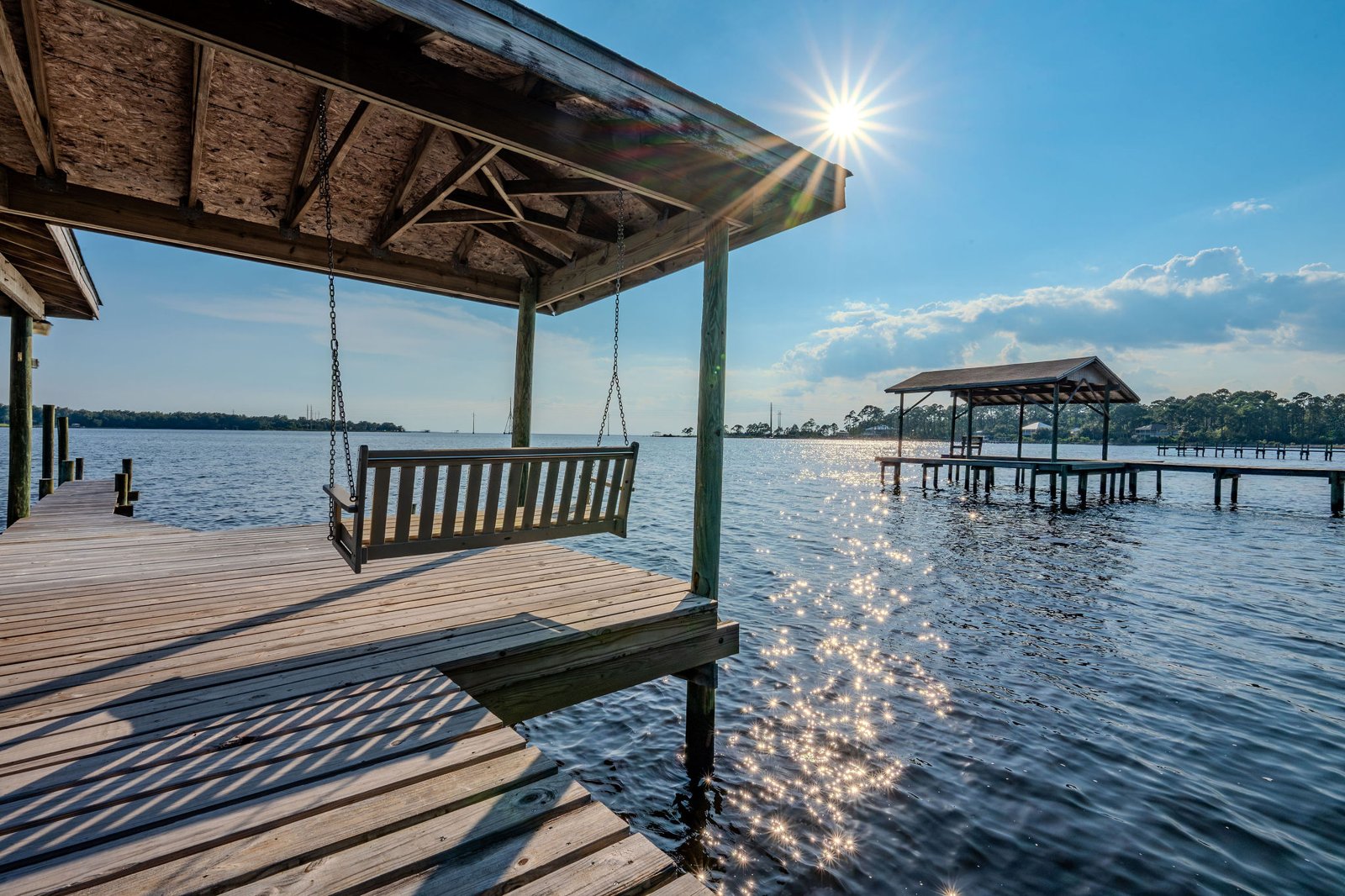 Covered dock with a porch swing looking out over sunlit water