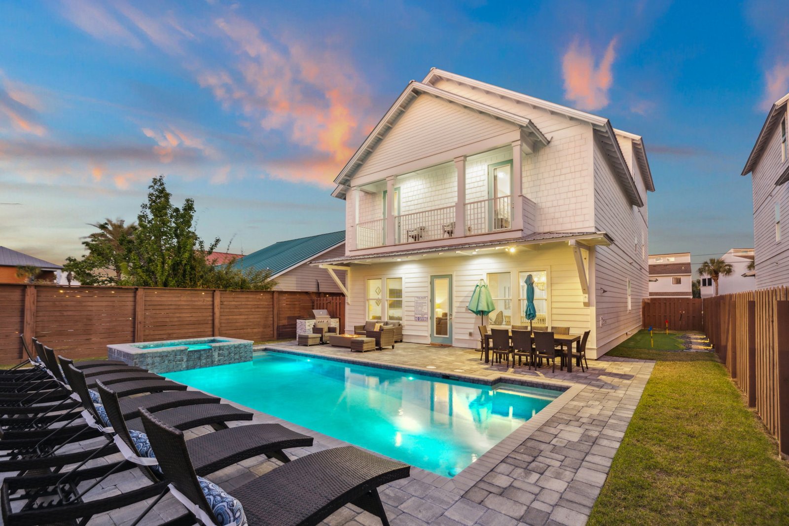 Two-story coastal home at dusk with a lit pool in the foreground